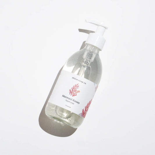 A clear pump bottle of Mermaid Kisses Eco-Friendly Liquid Soap by Shore Soap Co., adorned with a red coral graphic, rests on a white background and casts a soft shadow. Made with natural ingredients, this gentle hand soap is perfect for sensitive skin.