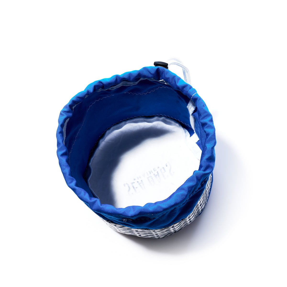 A top view of Sea Bags’ Anchor Pop Ditty Bag, a round, white woven basket featuring a blue sail cloth fabric lining and a drawstring closure reminiscent of classic ditty bags, set against a white background.
