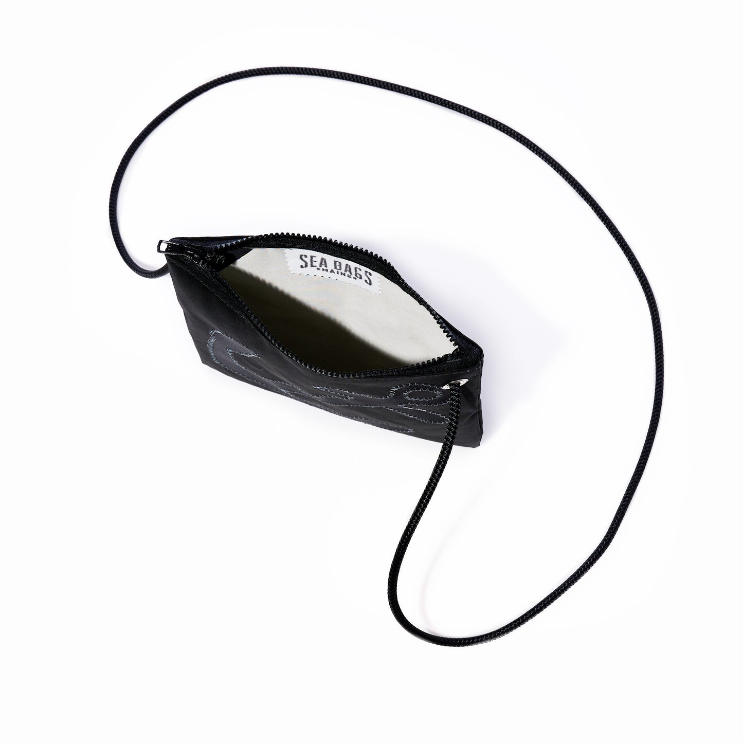 The Black-on-Black Anchor Slim Crossbody by Sea Bags is a small black zippered pouch featuring a thin, adjustable strap. Shown open to display its white interior label stamped with the Sea Bags brand, this hands-free bag is photographed against a white background. by Sea Bags