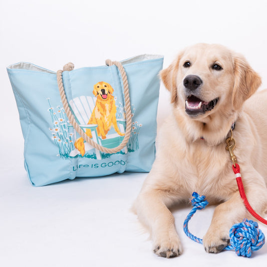 A golden retriever lies next to a light blue tote bag featuring an illustration of a golden retriever and the text Life is Good, with a Fetch ME Floating Rope Dog Toy - Blue peeking out from the bag. by Sea Bags