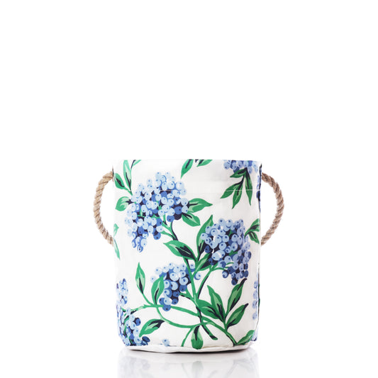 The Blueberry Print Bucket Bag by Sea Bags features a white recycled sail cloth construction adorned with a blue floral print inspired by Maine blueberries and sturdy rope handles, shown here on a white background. by Sea Bags