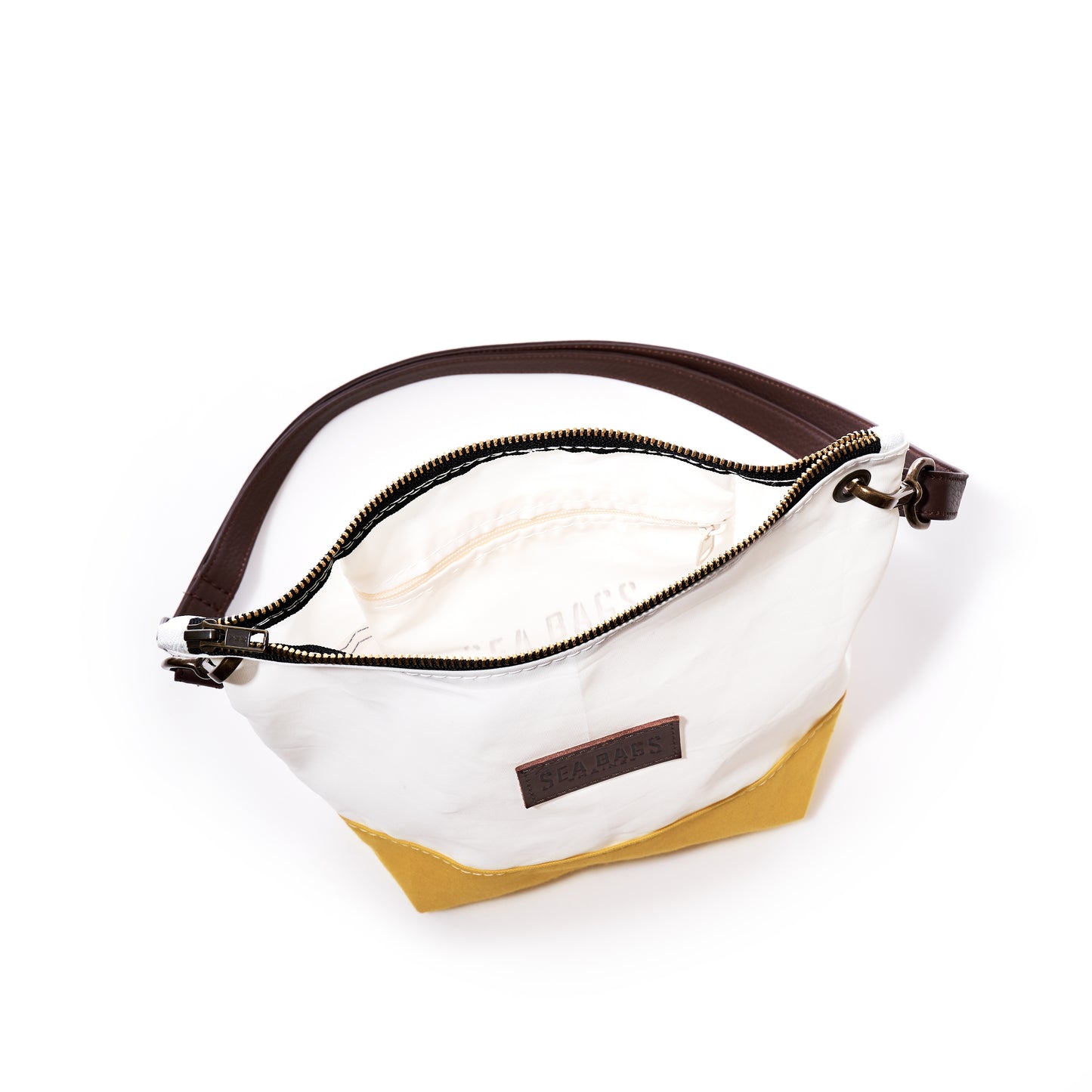 Golden yellow and white handbag with a dark handle, open top revealing an inner pocket and zipper, displayed on a white background. The Golden Yellow Chebeague Crossbody Bag by Sea Bags is crafted from recycled sailcloth and inspired by the rugged beauty of the Maine coast. by Sea Bags