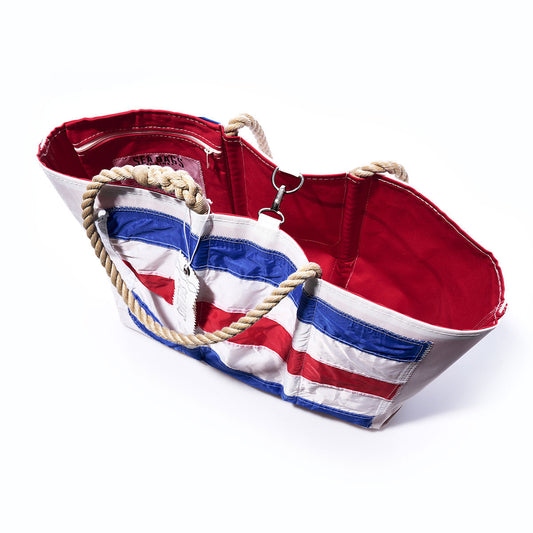 The Sea Bags Charlie Signal Flag Large Tote is a limited-edition bag featuring rope handles, a vibrant red interior, and an exterior adorned with blue, white, and red stripes inspired by maritime signal flags. It is photographed on a white background. by Sea Bags