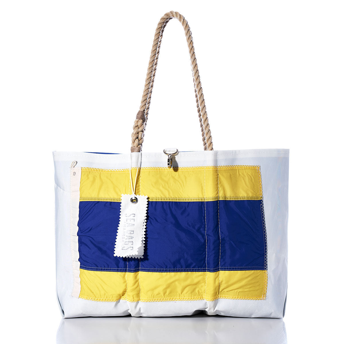 Introducing the Delta Signal Flag Large Tote from Sea Bags—a spacious tote with rope handles, crafted from recycled sail cloth. Showcasing a bold stitched yellow and blue rectangular design inspired by maritime signal flags, it features a white tag attached to one handle for added charm, blending nautical style with eco-friendly craftsmanship. by Sea Bags