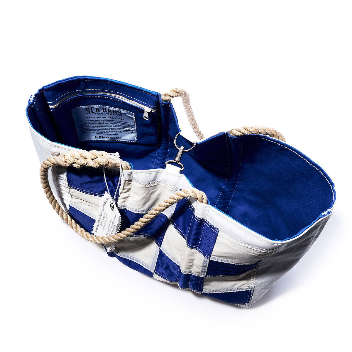 Sea Bags’ November Signal Flag Large Tote features blue and white recycled sail cloth, sturdy rope handles, an open design revealing a blue interior, a zippered white inside pocket, and a fabric brand label. by Sea Bags