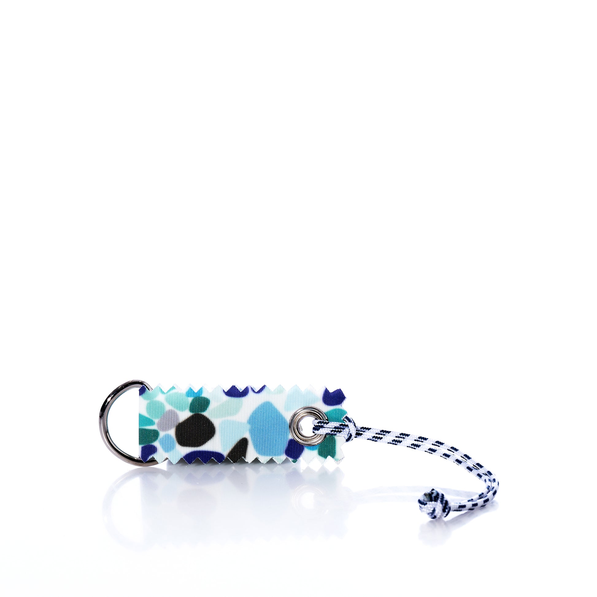 Sea Bags’ Sea Glass Print Sail Bag Charm features a rectangular design with a blue, black, and white abstract print, crafted from upcycled sail cloth for sustainable style. It is attached to a metal ring and finished with a blue-and-white cord, shown on a white background. by Sea Bags