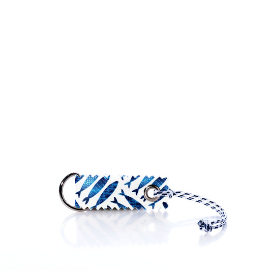 Introducing the Fish Print Sail Bag Charm by Sea Bags—a unique rectangular keychain crafted from upcycled sail cloth, featuring a distinctive blue and white fish pattern. Complete with a keyring and braided string, this eco-friendly accessory brings nautical flair and sustainable style to your collection. by Sea Bags