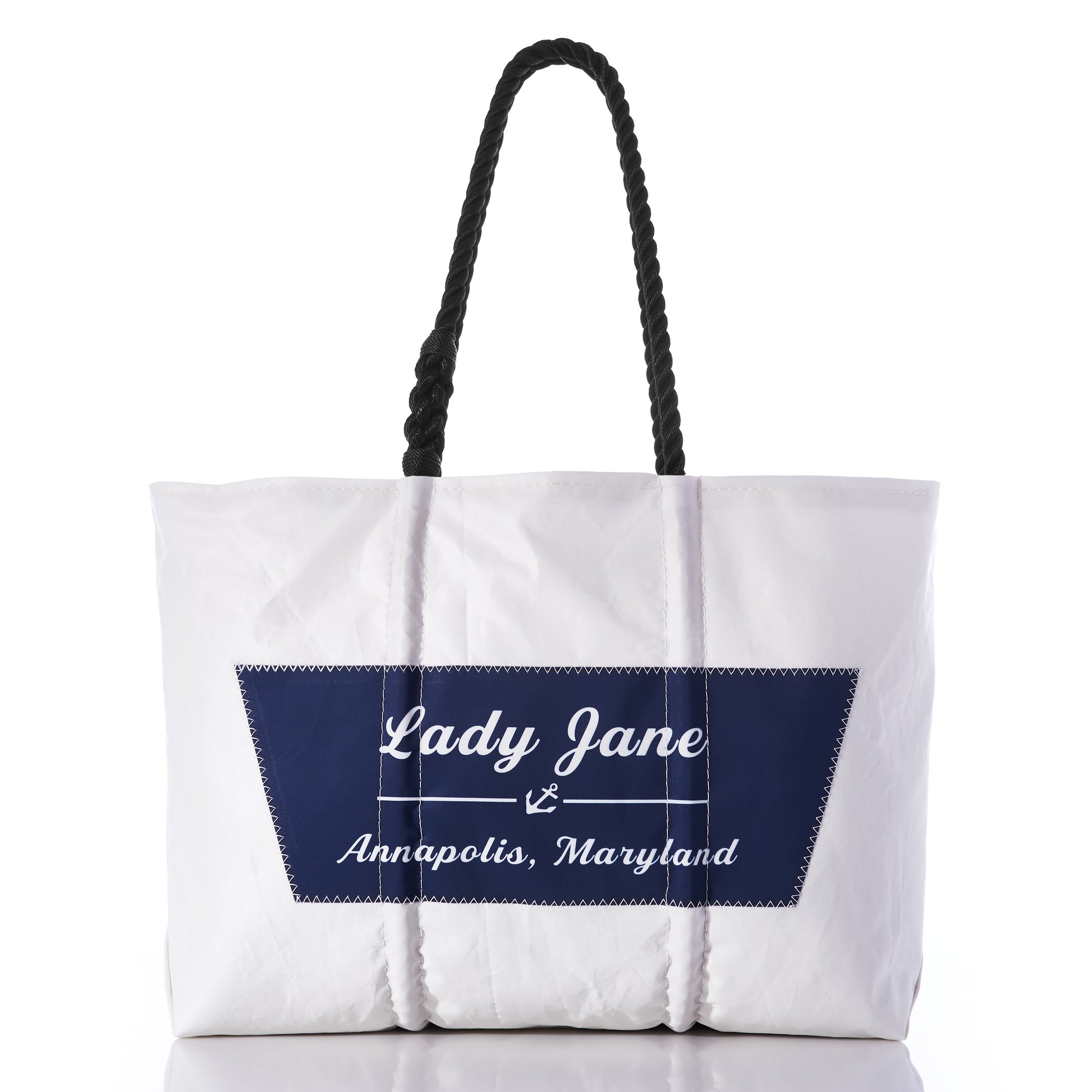 The Custom Boat Name Tote by Sea Bags is a white tote with black rope handles, featuring a blue patch with Lady Jane Annapolis, Maryland in white script—a classic personalized boat tote perfect for displaying your boat’s name in style. by Sea Bags