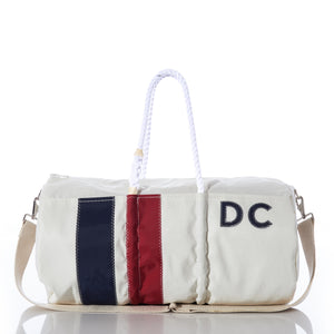 The Sea Bags Custom Monogram Vertical Stripe Duffel, photographed on a reflective surface, features white recycled sail cloth adorned with navy and red vertical stripes, rope handles, a beige shoulder strap, and stitched DC initials. This stylish gym bag blends durability with eco-friendly charm for a personalized touch. by Sea Bags