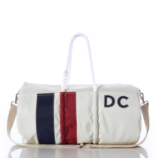The Sea Bags Custom Monogram Vertical Stripe Duffel, photographed on a reflective surface, features white recycled sail cloth adorned with navy and red vertical stripes, rope handles, a beige shoulder strap, and stitched DC initials. This stylish gym bag blends durability with eco-friendly charm for a personalized touch. by Sea Bags