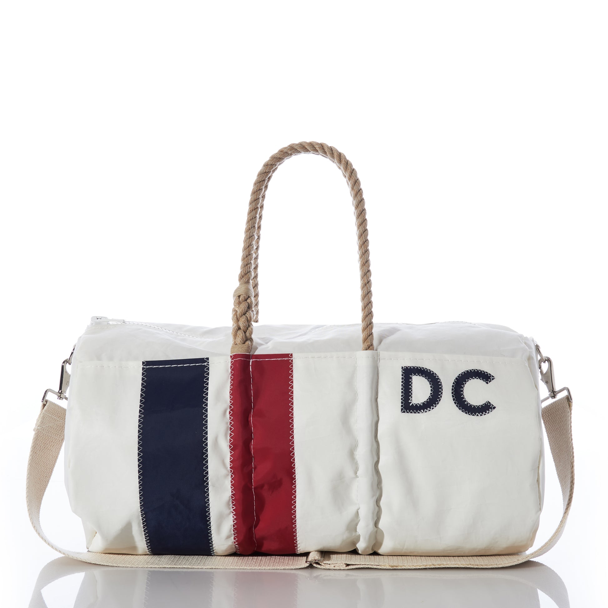 Sea Bags Custom Monogram Vertical Stripe Duffel, crafted from recycled sail cloth and photographed on a white background, features beige rope handles, a beige shoulder strap, a navy and red vertical stripe, and “DC” monogrammed on the front—a stylish and durable choice for any adventure. by Sea Bags