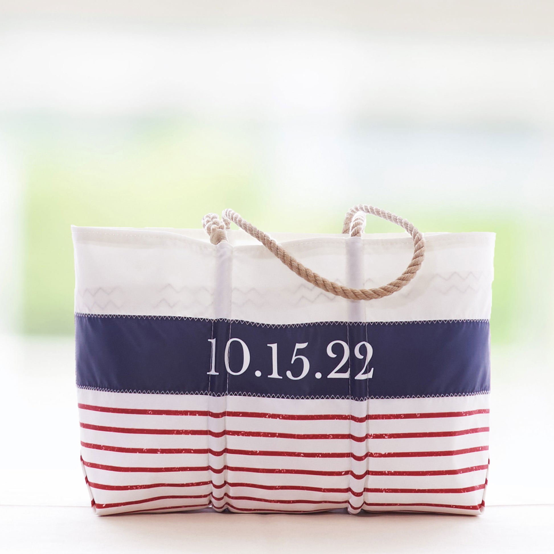 The Sea Bags Custom Mariner Stripe Tote features a nautical design with red stripes, a blue stripe, and sturdy rope handles. Crafted from recycled sail cloth for style and sustainability, this white tote can be personalized with the date 10.15.22 printed on the front. by Sea Bags
