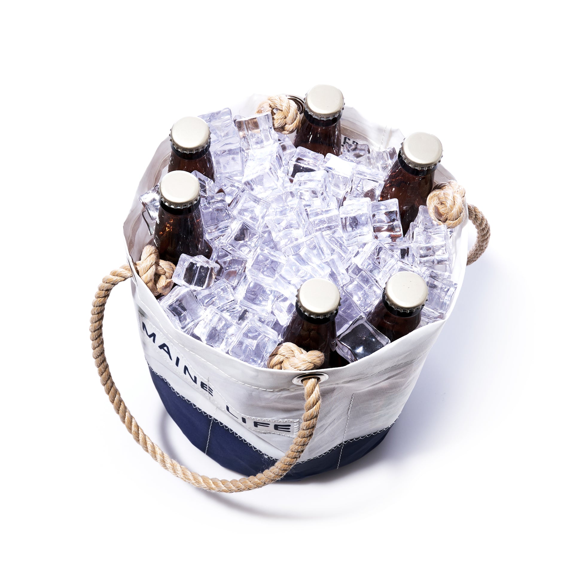 Six brown glass bottles are nestled in the Maine Life Beverage Bucket by Sea Bags—a white beverage bucket crafted from recycled sail cloth and finished with rope handles—filled with ice cubes and photographed against a white background, offering a refreshing tribute to Maine life. by Sea Bags