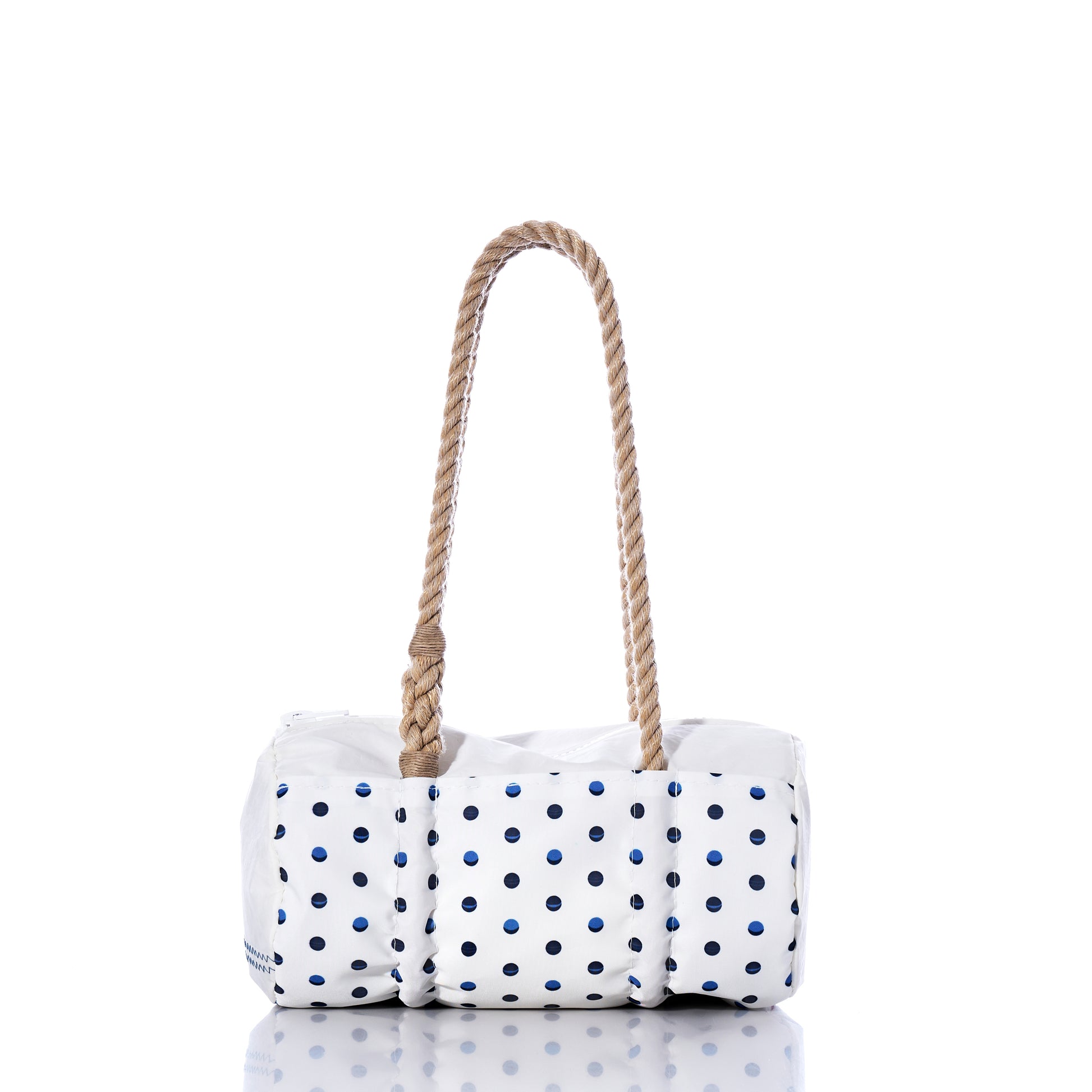 The Flip Side Summer Dots Baguette Bag by Sea Bags features a white design adorned with navy blue polka dots and two thick, twisted rope handles. Photographed on a white background with a subtle reflection below, this chic summer handbag blends charm and practicality—ideal for sunny day outings. by Sea Bags