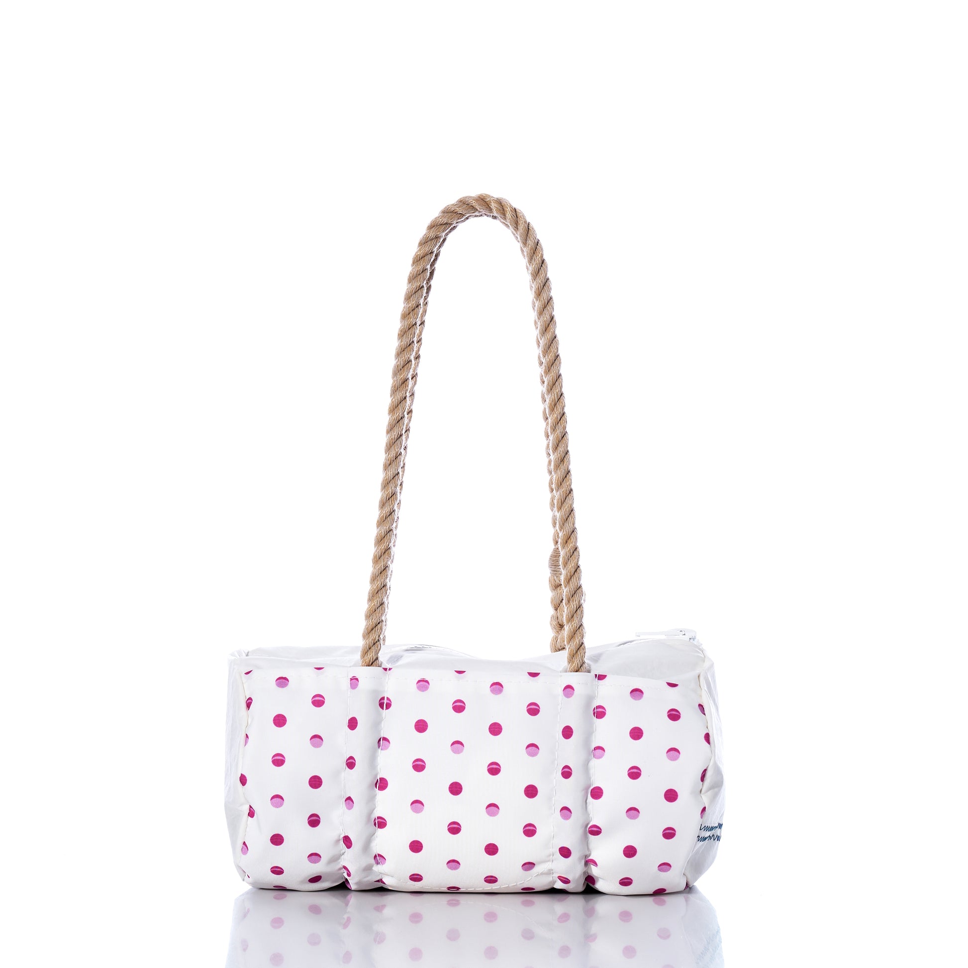 The Flip Side Summer Dots Baguette Bag by Sea Bags features a white tote design adorned with pink polka dots, a cushioned body, and two brown rope handles. Displayed on a reflective surface against a white background, this charming summer handbag blends playful style with everyday practicality. by Sea Bags