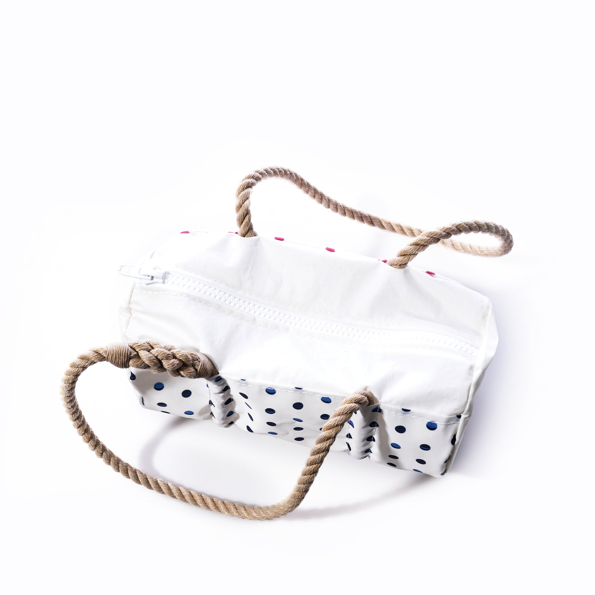 The Flip Side Summer Dots Baguette Bag by Sea Bags features a white zippered design with a blue polka dot bottom and thick, twisted rope handles, inspired by classic sailcloth baguette styles. Displayed on a white background, its the perfect handbag for summer. by Sea Bags