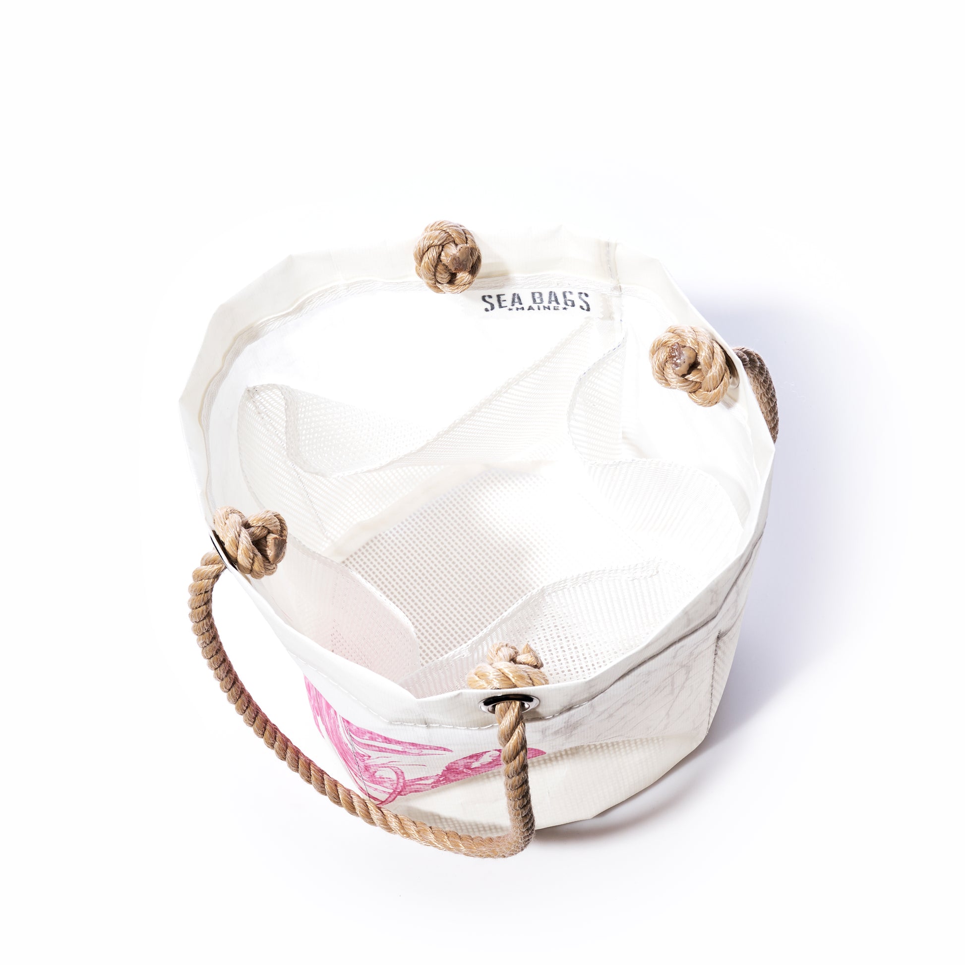 The Pink Lobster Beachcomber Bucket by Sea Bags is a white canvas beach bag crafted from recycled sail cloth, featuring sturdy rope handles with large knotted loops. The Sea Bags logo accents the inner rim, while a pink lobster design adds a distinctive touch to the exterior. This unique bucket bag blends style and sustainability—perfect for your seaside adventures. by Sea Bags