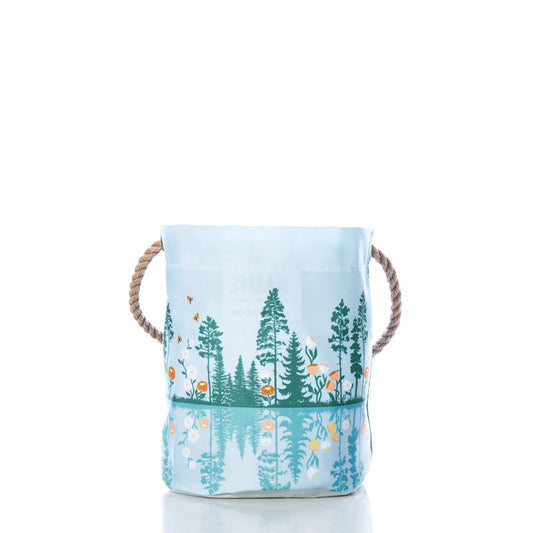 Sea Bags Life is Good Lakeside Sunset Bucket features a light blue fabric design with rope handles, adorned with green trees and orange flowers reflected along the bottom—all set against a white background. This charming Maine-inspired organizer makes a delightful housewarming gift. by Sea Bags