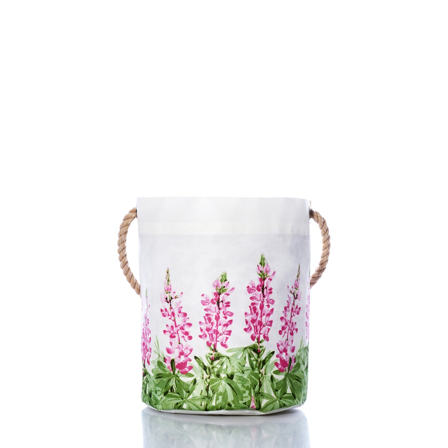Sea Bags Pink Lupine Bucket features white fabric and sturdy rope handles, accented by a pink and green floral pattern near the base. Shown on a reflective surface with a white background, this stylish bucket adds a fresh touch of spring décor to any room. by Sea Bags
