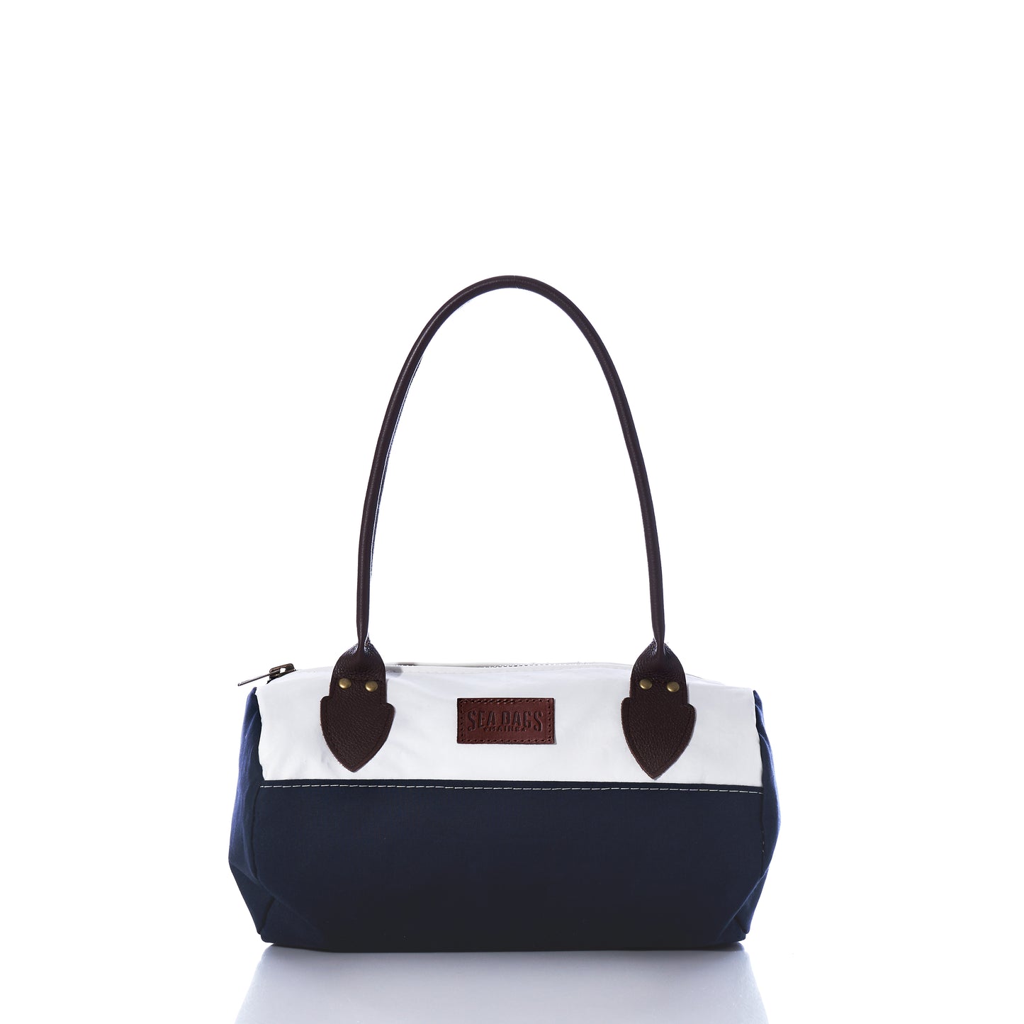 The Chebeague Baguette Bag by Sea Bags is a small, two-tone handbag crafted from recycled sailcloth, featuring a dark blue bottom, white top section, brown handles, and a visible rectangular Sea Bags label on the front. by Sea Bags