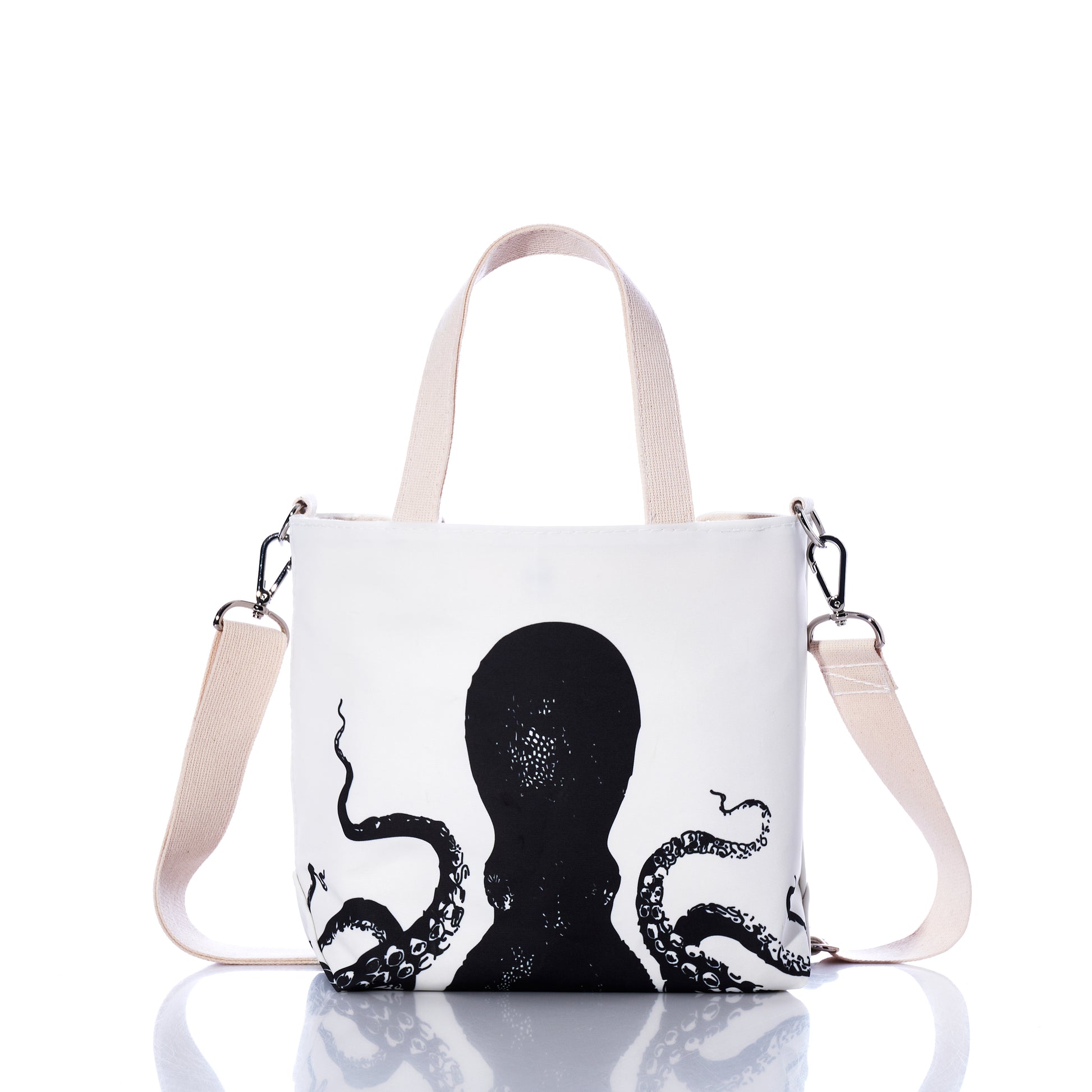 The Sea Bags Octopus Crossbody Tote, crafted from recycled sailcloth, features a black octopus illustration, beige handles, and an adjustable beige shoulder strap, and is displayed on a reflective surface. by Sea Bags