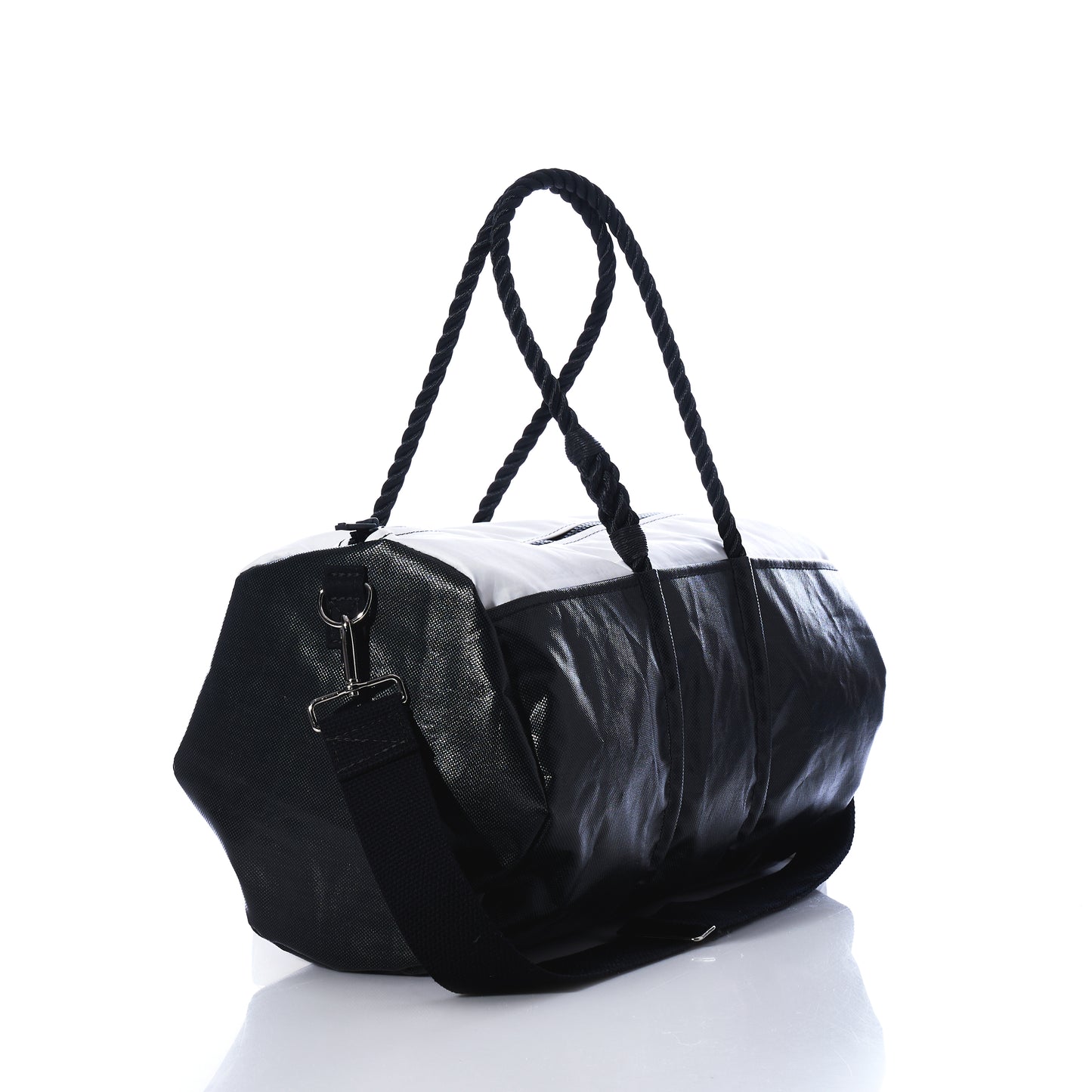 The Sea Bags Black Dragon Duffel, crafted from water-resistant recycled sail cloth, features rope handles and an adjustable shoulder strap. Photographed on a white background with a light reflection, this black and white travel bag combines durability with distinctive maritime style. by Sea Bags