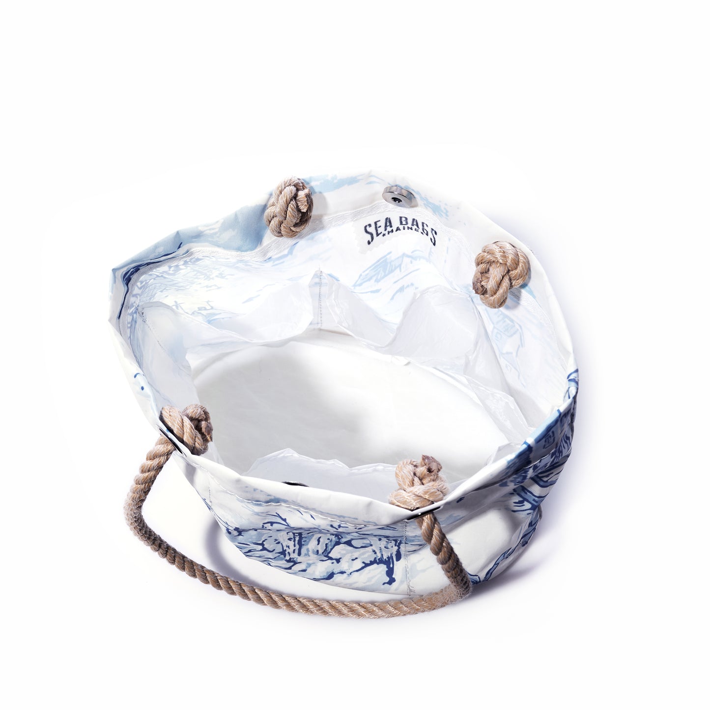 The Maine Fishing Village Essential Handbag by Sea Bags, crafted from recycled sail cloth and featuring white and blue canvas with rope handles and knotted corners, is inspired by the Maine coast. The SEA BAGS label is displayed on the inner lining, and the bag is photographed against a white background. by Sea Bags