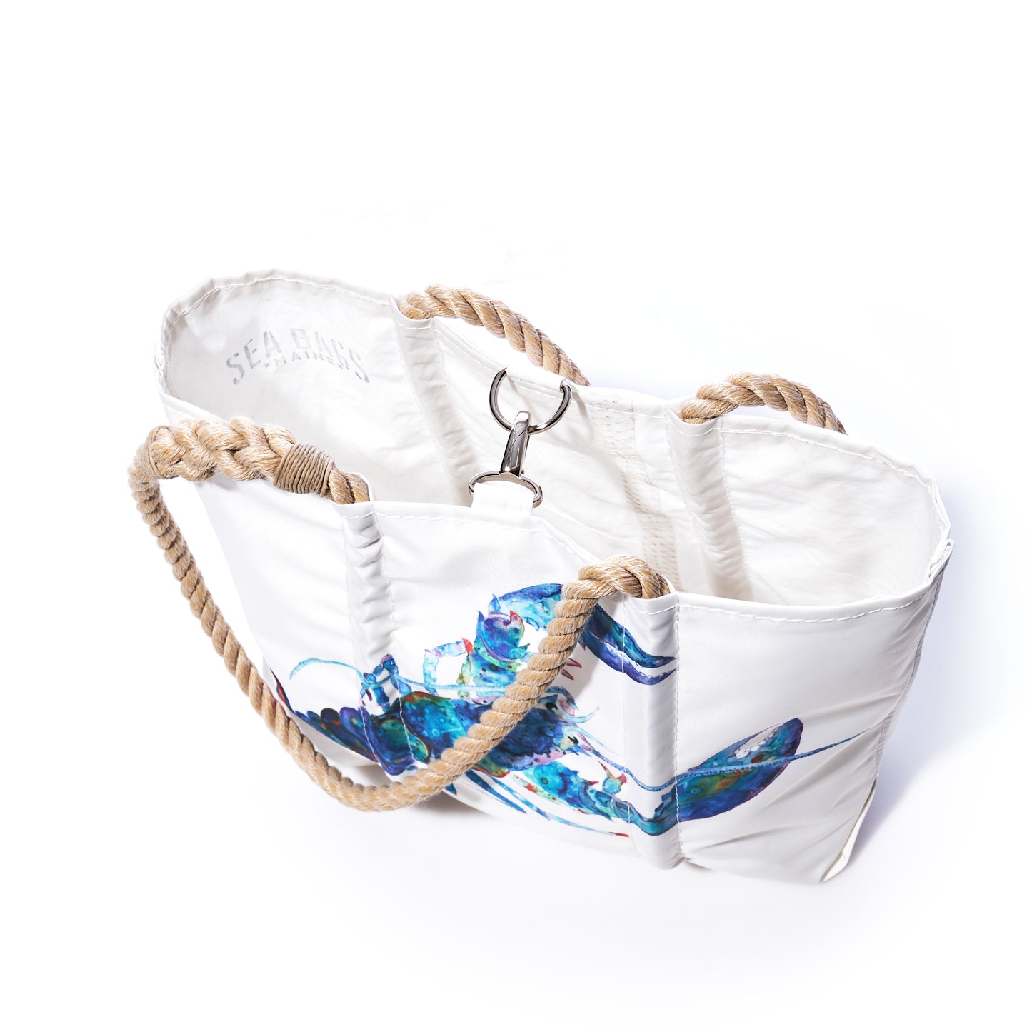 Introducing the Multicolor Lobster Handbag by Sea Bags—a white tote crafted from recycled sail cloth with rope handles and a metal clasp. This sustainable handbag features a vibrant cotton candy lobster illustration by a Maine artist, blending coastal style with eco-friendly design. by Sea Bags