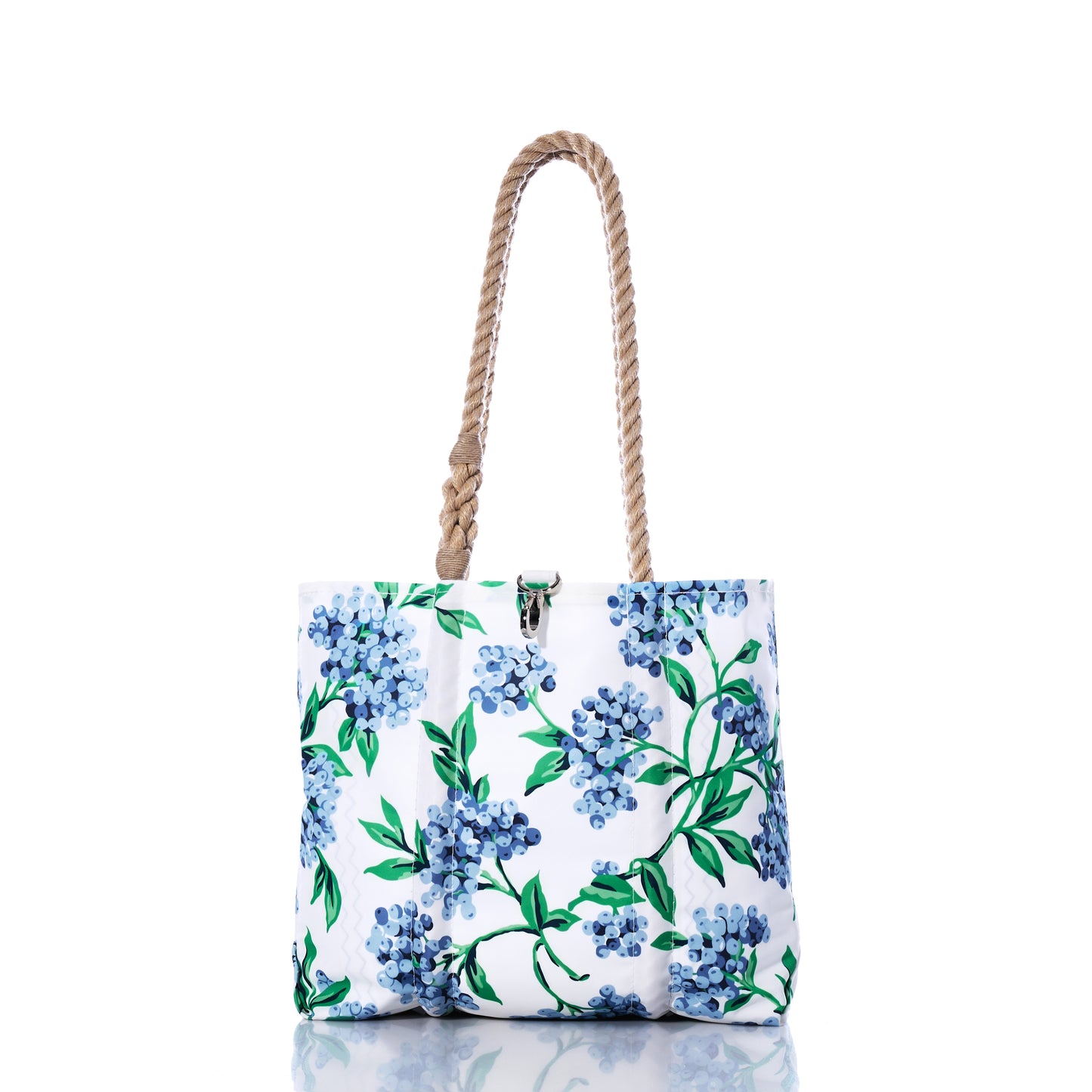 The Blueberry Print Handbag by Sea Bags showcases a blue and green floral motif inspired by Maine blueberries, is crafted from recycled sail cloth, and features two braided rope handles—its versatile design is beautifully displayed on a reflective white surface. by Sea Bags