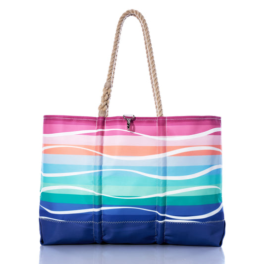 The Sunset Surf Ogunquit Beach Tote by Sea Bags is a spacious tote bag featuring sturdy rope handles and a vibrant wave pattern in pink, orange, aqua, and blue on a crisp white background. Thoughtfully designed for convenience, it includes waterproof pockets to keep your essentials safe and dry. by Sea Bags