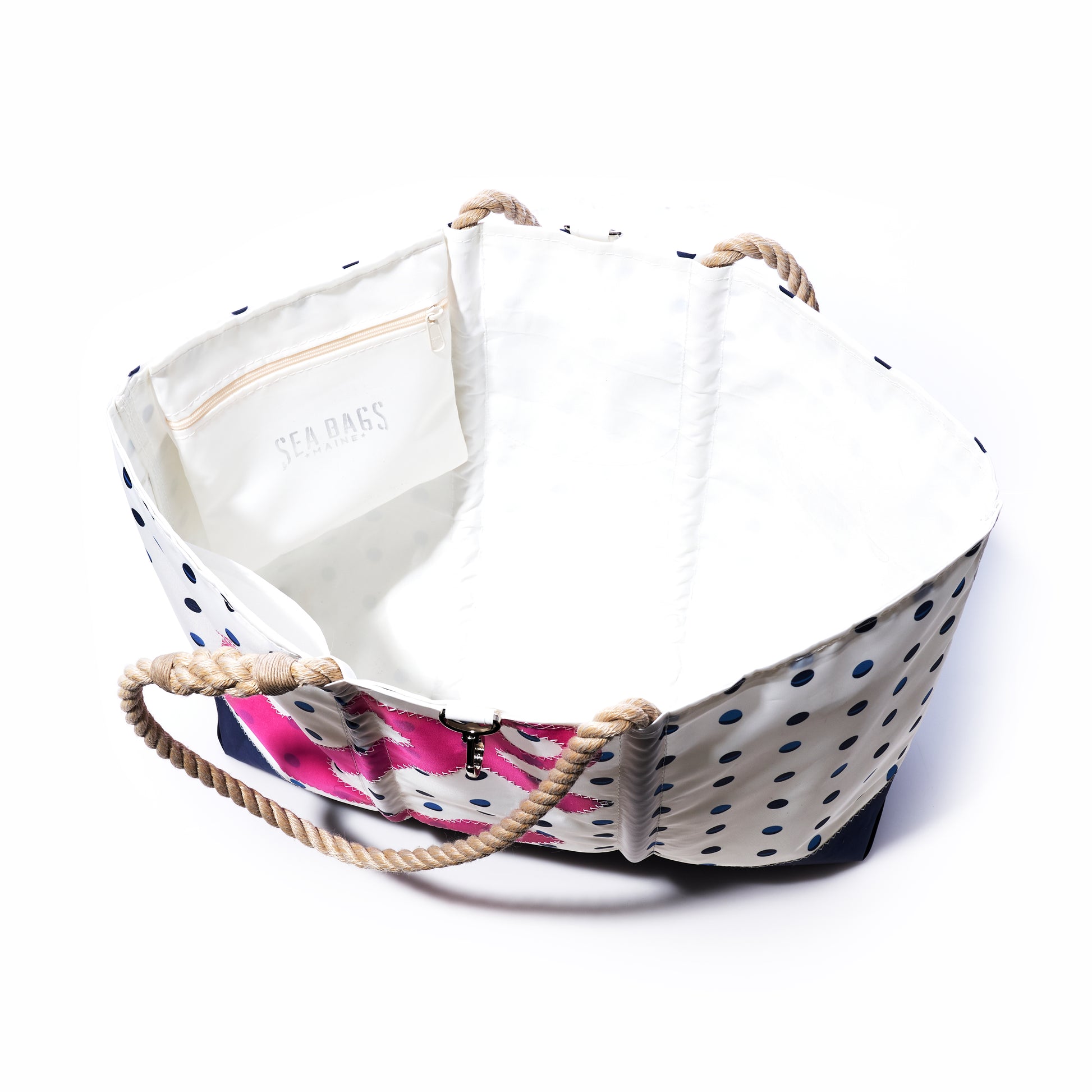 Introducing the Fuchsia Anchor  Summer Dots Ogunquit Beach Tote by Sea Bags, crafted from recycled sail cloth with a vibrant mix of white and blue polka-dot canvas, sturdy rope handles, and a fuchsia-patterned side. This stylish tote includes an interior pocket adorned with the Sea Bags logo, all showcased against a plain white background. by Sea Bags