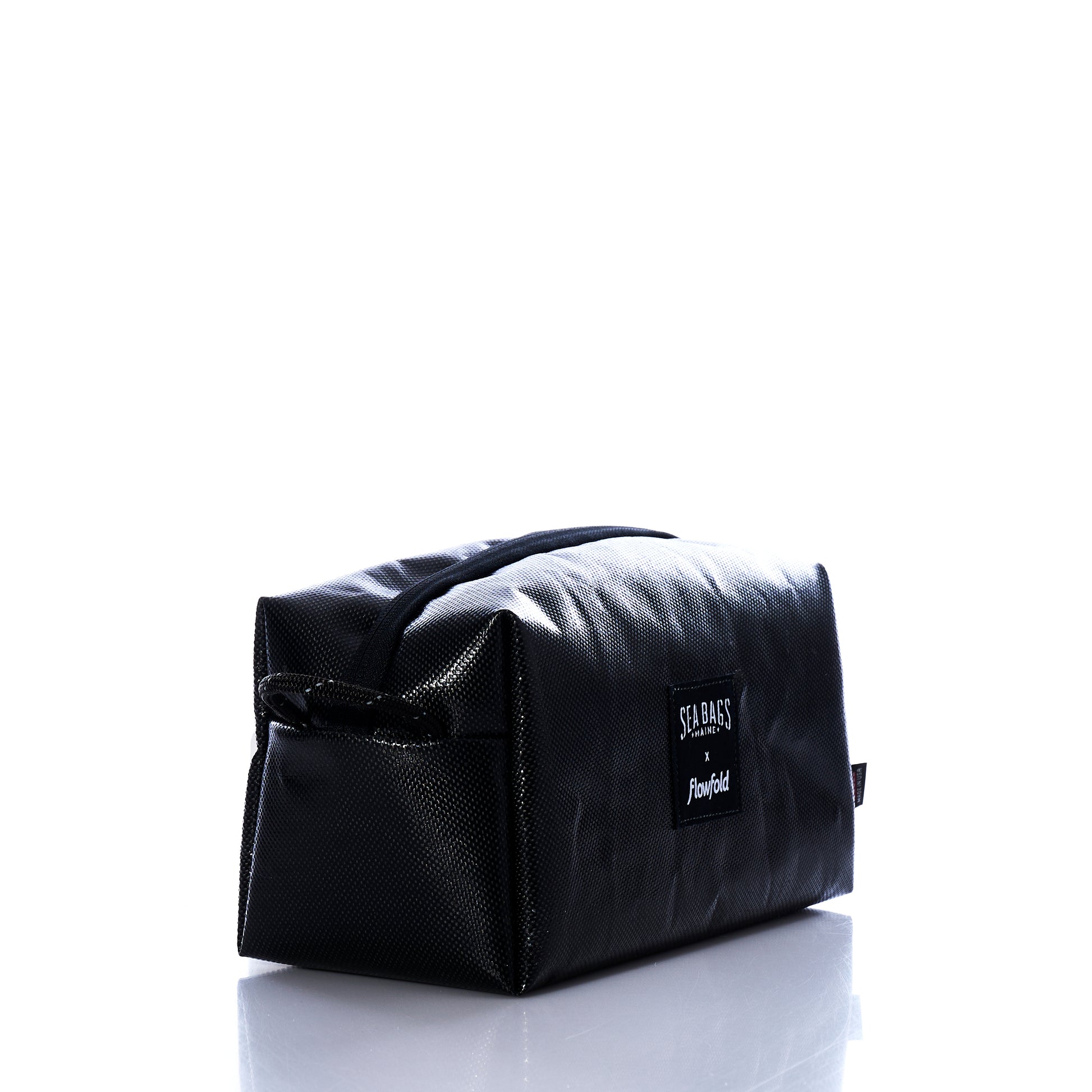 Black Dragon Toiletry Bag by Sea Bags—this rectangular, black toiletry kit features a sturdy handle and a visible Sea Bags label, shown against a white background with a soft reflection beneath. Crafted from water-resistant material, it makes a unique gift for any traveler. by Sea Bags