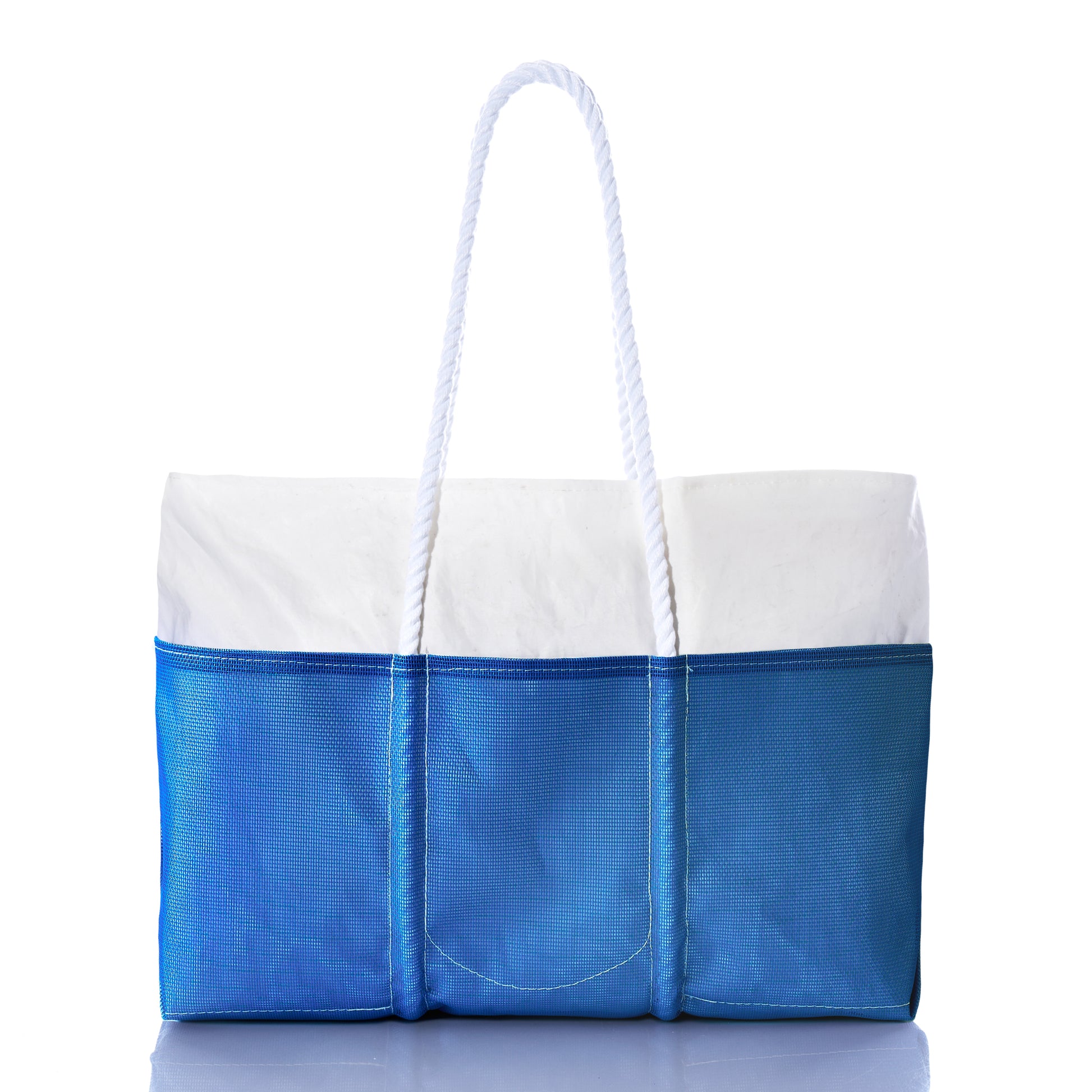 The Sea Bags Harbor Blue Beachcomber Tote—a rectangular beach bag featuring a white top, blue bottom, exterior pockets, and two white rope handles—is displayed against a white background. by Sea Bags
