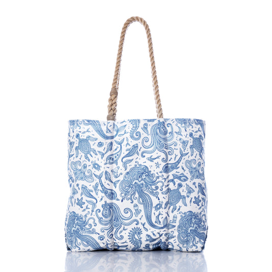 Paisley Mermaid Medium Tote by Sea Bags—a white tote bag adorned with blue, ocean-inspired paisley mermaid, fish, and seashell illustrations. Features two twisted rope handles for a nautical beach bag look. Photographed on a white background with a subtle reflection. by Sea Bags