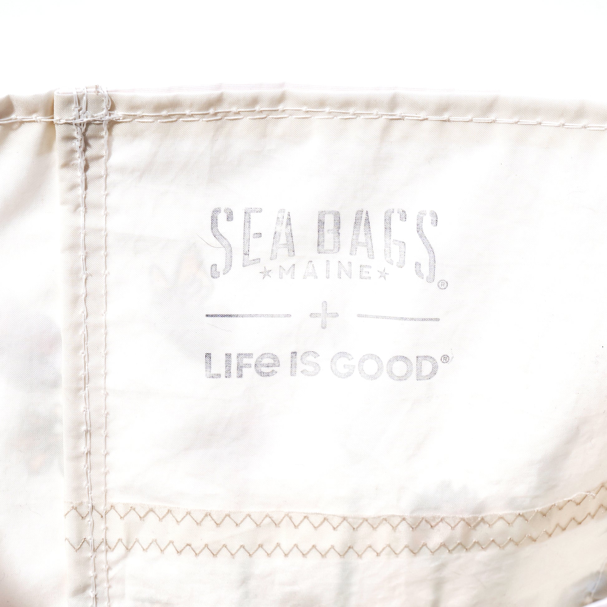 Handcrafted in Maine from recycled sail bag materials, the Life is Good Wildflowers Medium Tote by Sea Bags features white fabric with visible stitching and is printed with faded gray SEA BAGS MAINE and LIFE IS GOOD logos. by Sea Bags