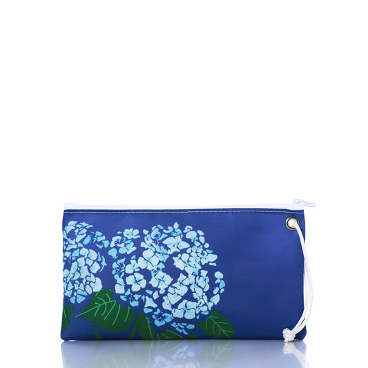 The Harbor Blue Hydrangea Large Wristlet by Sea Bags is a blue zippered pouch crafted from recycled sail cloth, featuring a white string and a hydrangea flower design on the front, shown on a reflective white background—an ideal coastal accessory to enhance your collection. by Sea Bags