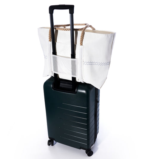 A white Sea Bags Trolley Sleeve Travel Tote, crafted from recycled sailcloth with sturdy rope handles and a breathable mesh trolley sleeve, is securely attached to the handle of a dark green four-wheeled rolling suitcase against a white background. by Sea Bags