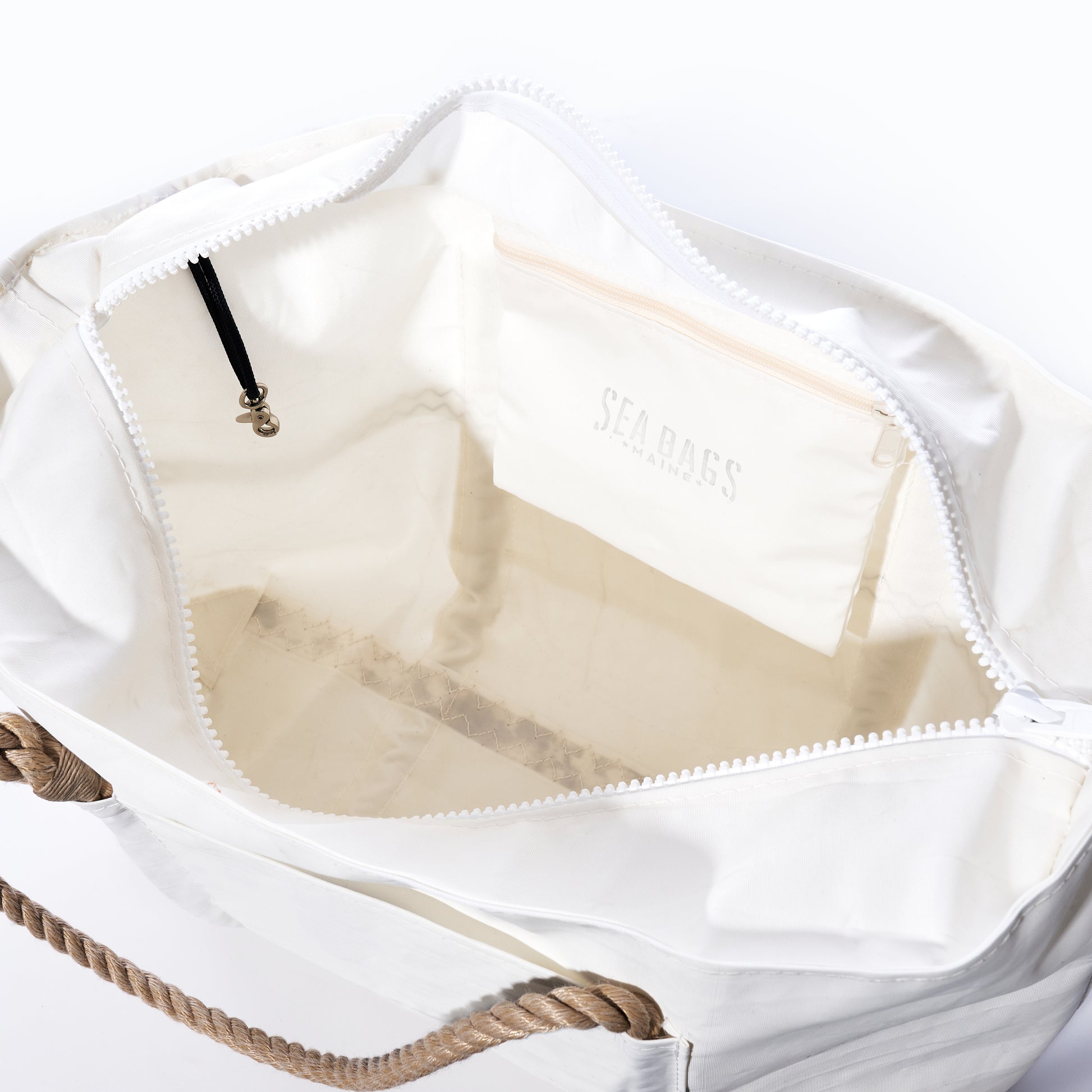 The Trolley Sleeve Travel Tote by Sea Bags is crafted from recycled sailcloth in open white and features a mesh trolley sleeve, rope handle, zippered top, and an interior pocket labeled with the Sea Bags logo. by Sea Bags