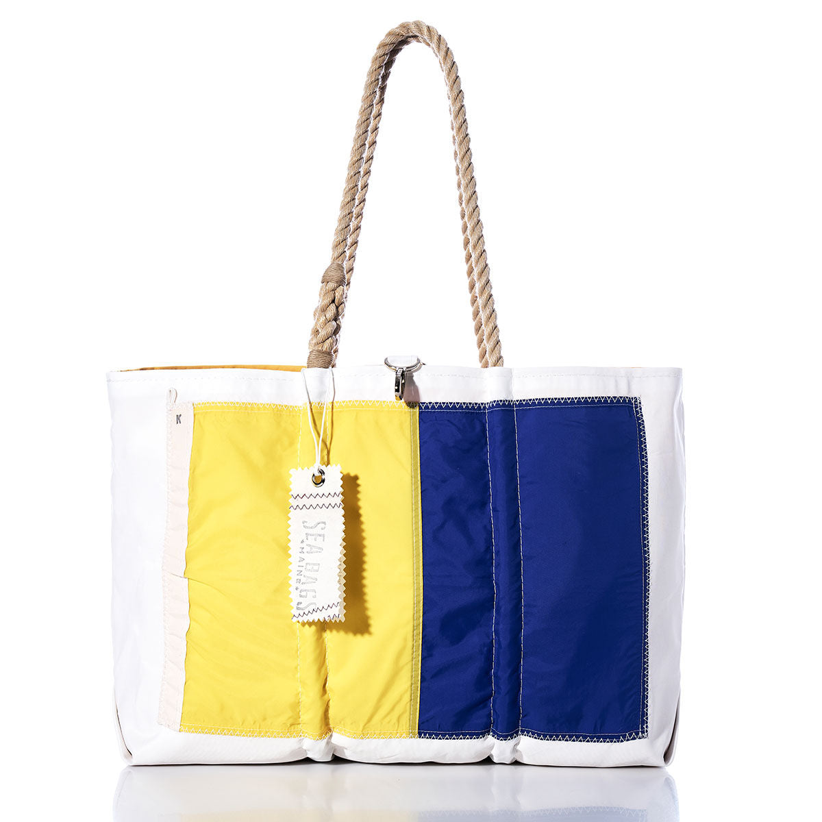 The Kilo Signal Flag Large Tote by Sea Bags is a spacious maritime tote crafted from recycled sail cloth, showcasing blue, yellow, and white panels inspired by vintage signal flags. Nautical rope handles, visible stitching, and a rectangular Sea Bags tag attached to one handle complete the design. by Sea Bags