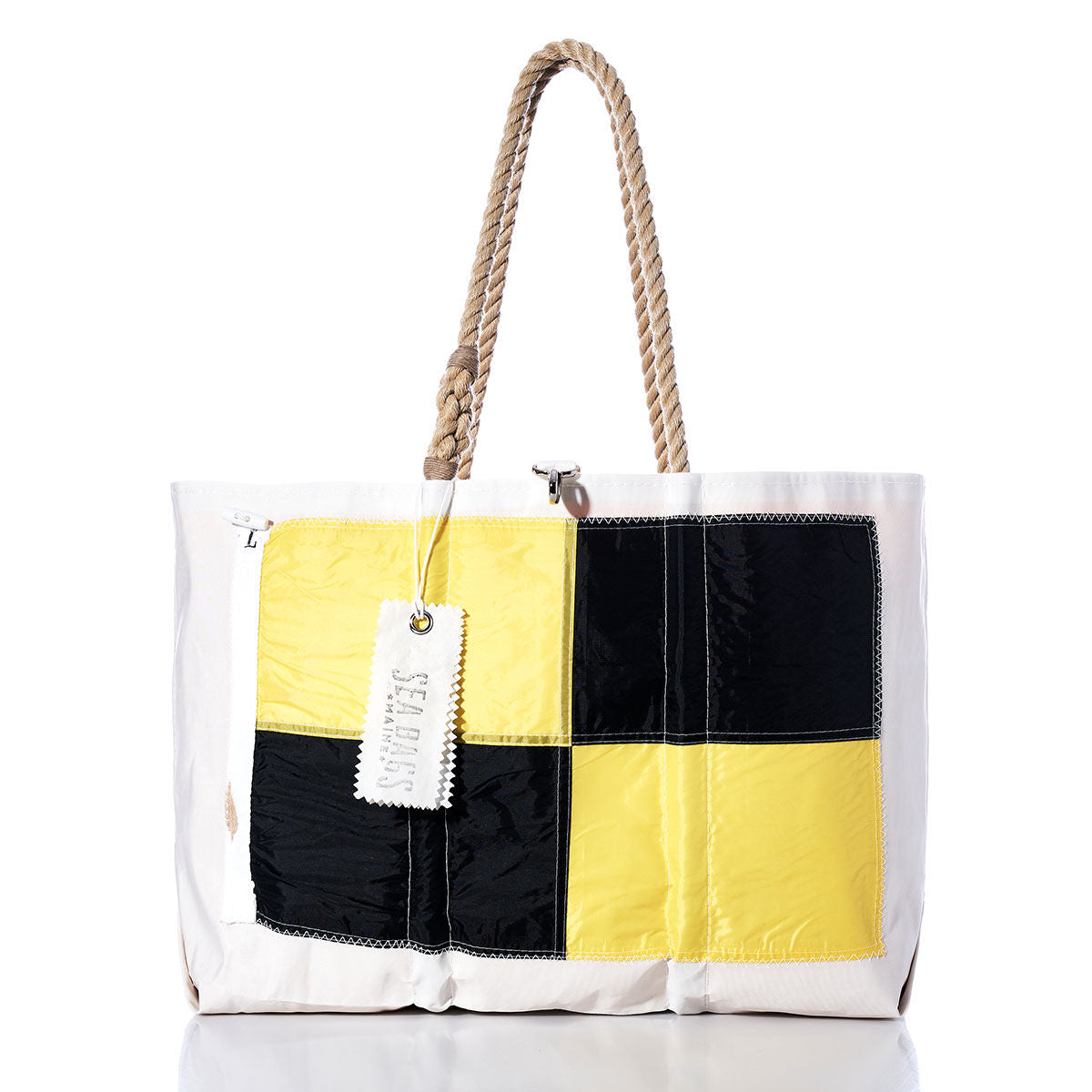 The Lima Signal Flag Large Tote by Sea Bags is a white tote bag made from recycled sail cloth, featuring sturdy rope handles, a yellow and black checkered patch inspired by vintage signal flags, and a rectangular SEA BAGS tag. by Sea Bags