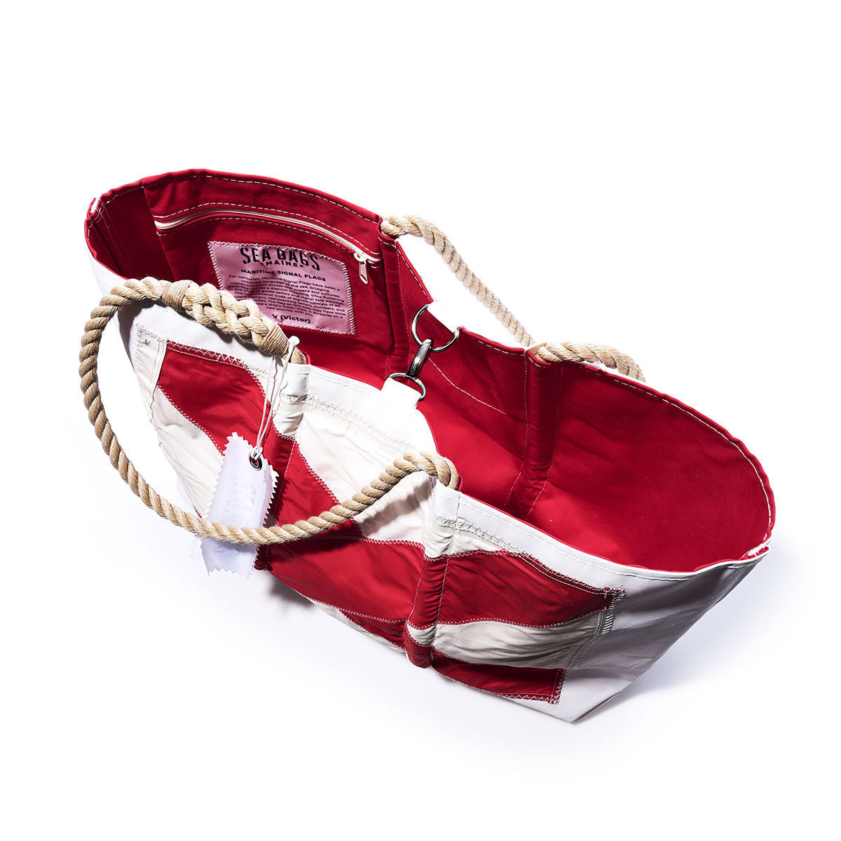 The Victor Signal Flag Large Tote by Sea Bags is a red and white canvas bag with rope handles, crafted from recycled sail cloth, shown open to reveal the interior and a sewn-in SEA BAGS label. by Sea Bags