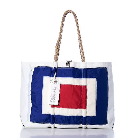 The Whisky Signal Flag Large Tote by Sea Bags is a handcrafted white tote bag featuring rope handles, adorned with blue and red rectangular patches inspired by maritime signal flags, and accented with a “SEABAGS” metal keychain. Made from vintage sail cloth, this stylish accessory combines nautical charm with lasting durability. by Sea Bags