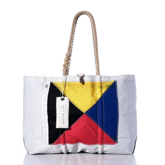 Introducing the Zulu Signal Flag Large Tote by Sea Bags—a white tote crafted from recycled sail cloth, featuring sturdy thick rope handles and a bold geometric pattern in yellow, blue, red, and black on the front, inspired by Maritime Signal Flags. A signature white tag is attached. by Sea Bags
