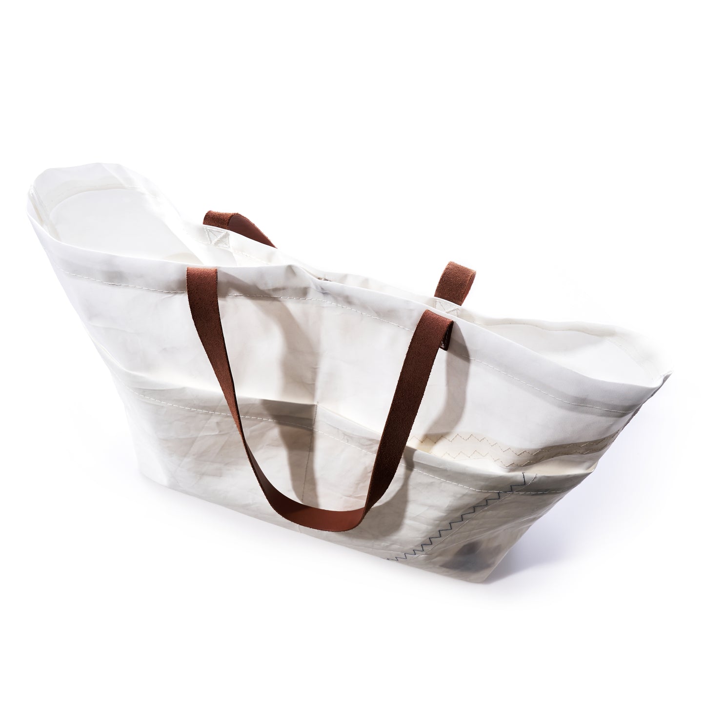 The Sea Bags Large Market Tote, crafted from white recycled sail material with brown leather handles, is displayed at an angle on a white background. The empty tote is lightweight and features a slightly translucent finish. by Sea Bags