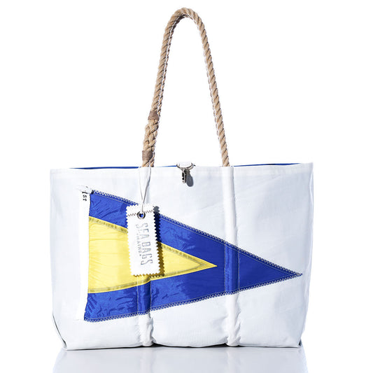 Sea Bags 1st Repeat Signal Flag Large Tote is a white bag with rope handles, crafted from recycled sail cloth and featuring a bold blue and yellow pennant design inspired by maritime signal flags on the front, finished with a white tag near the handle. by Sea Bags