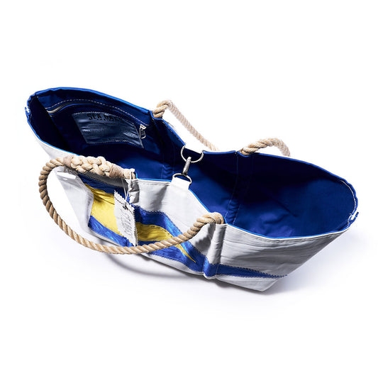 The Sea Bags 1st Repeat Signal Flag Large Tote, crafted from recycled sail cloth and inspired by vintage signal flag designs, features a blue and white exterior with yellow accents, a blue interior, rope handles, and a clasp closure, displayed on a white background. by Sea Bags