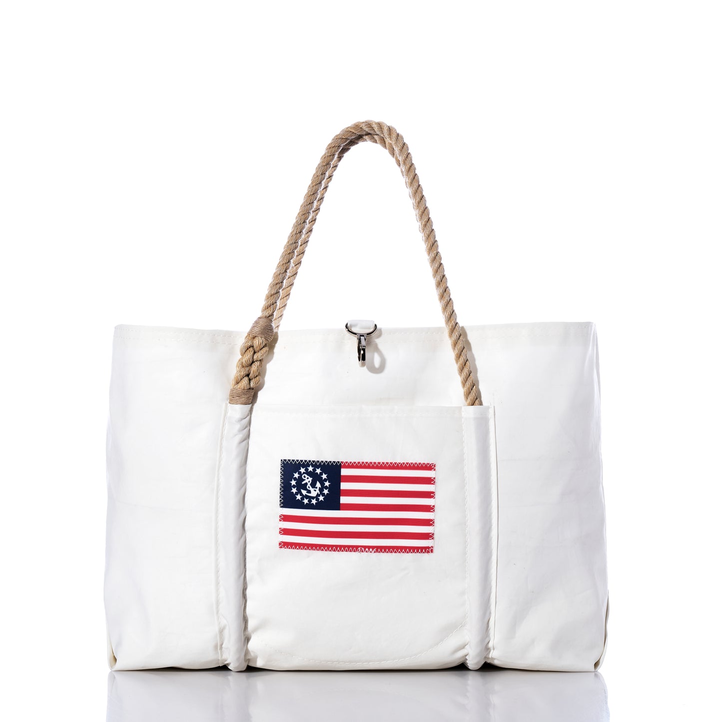 The U.S. Yacht Ensign Wharf Tote by Sea Bags is a white tote bag with rope handles, crafted from recycled sail cloth and featuring a vintage American flag patch with a circle of stars on the front pocket. Displayed against a plain white background, this piece blends sustainable craftsmanship with classic nautical style. by Sea Bags