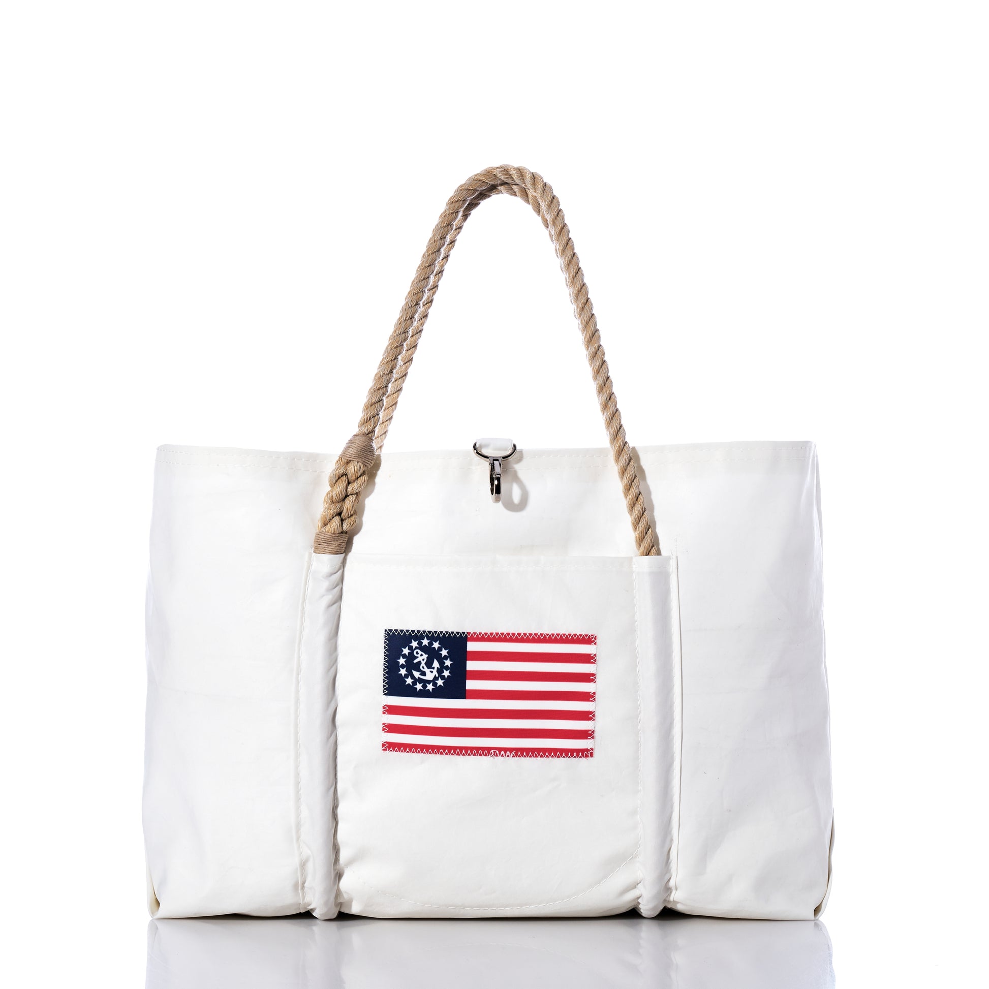 The U.S. Yacht Ensign Wharf Tote by Sea Bags is a white tote bag with rope handles, crafted from recycled sail cloth and featuring a vintage American flag patch with a circle of stars on the front pocket. Displayed against a plain white background, this piece blends sustainable craftsmanship with classic nautical style. by Sea Bags