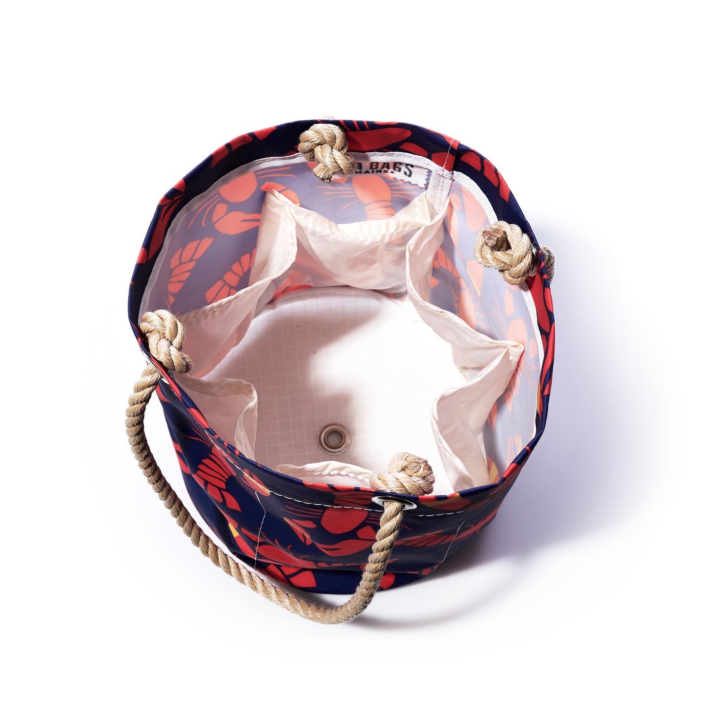 Top view of the Sea Bags Lobster Bake Beverage Bucket, an open, round recycled sail cloth bag featuring rope handles, a white interior lining, a lobster and floral exterior pattern, and multiple inner pockets. by Sea Bags
