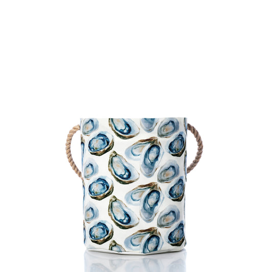The Watercolor Oyster Bucket by Sea Bags is a white cylindrical container made from recycled sail cloth, adorned with an eye-catching blue watercolor oyster print and finished with rope handles on both sides—capturing the coastal charm of a bucket bag against a crisp white background. by Sea Bags